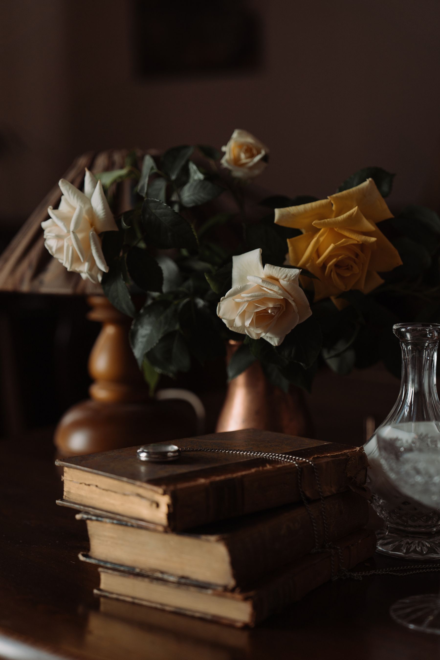 Cream roses in a brass pitcher beside a stack of antique books in warm light